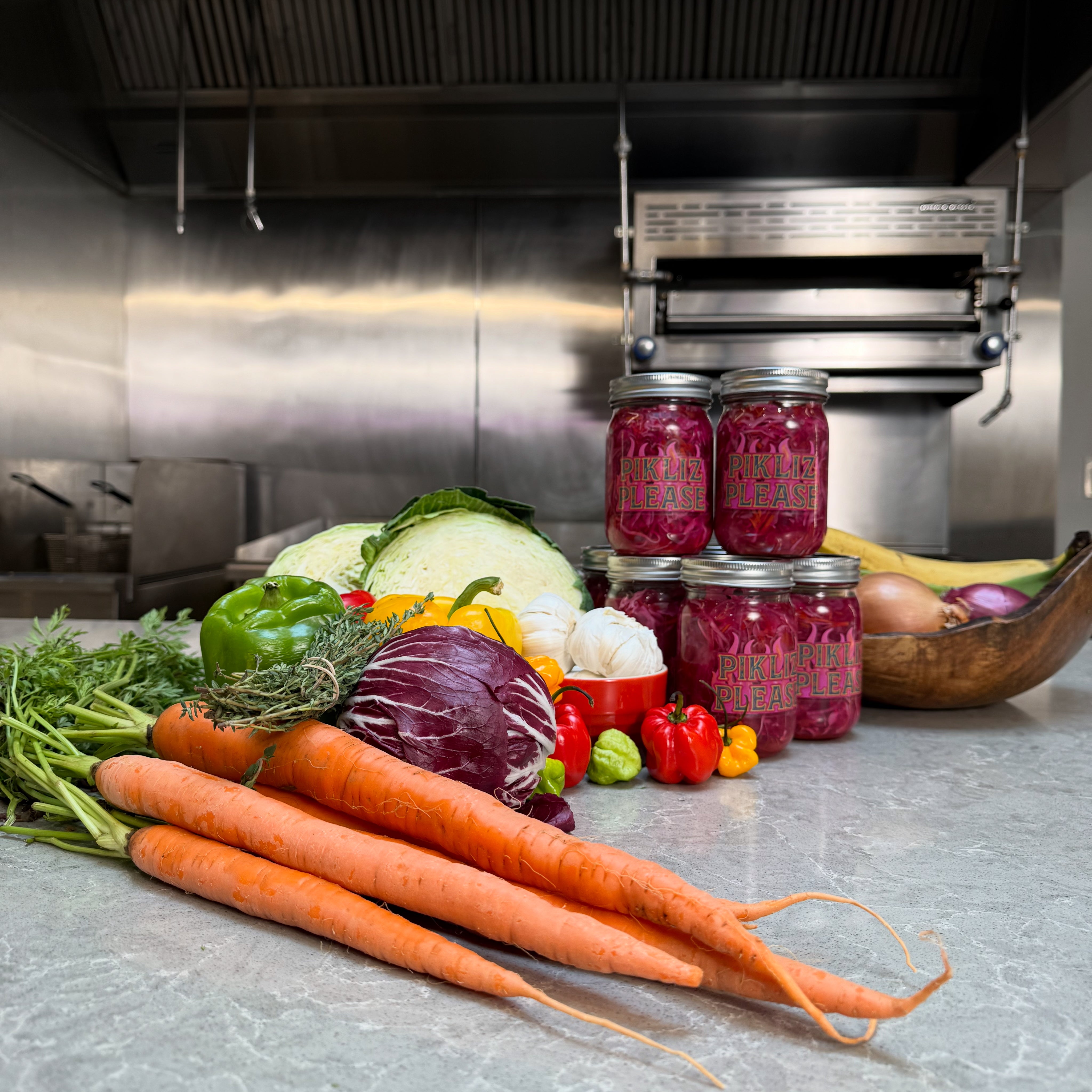 Jars of Pikliz Please on a kitchen counter with vegetables