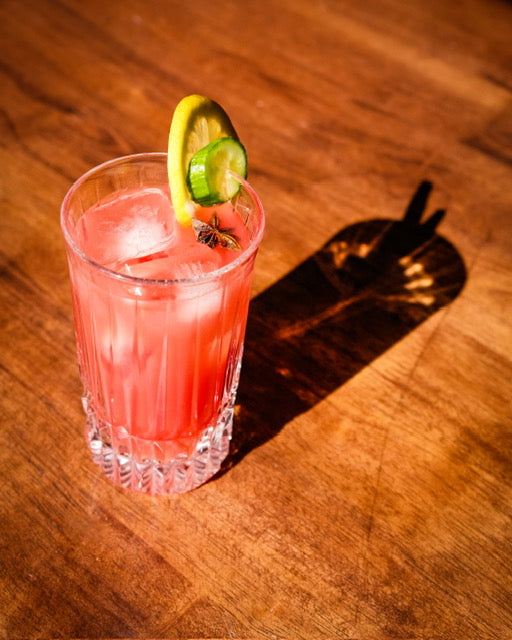 Pink cocktail with a lemon and lime garnish on a wooden surface