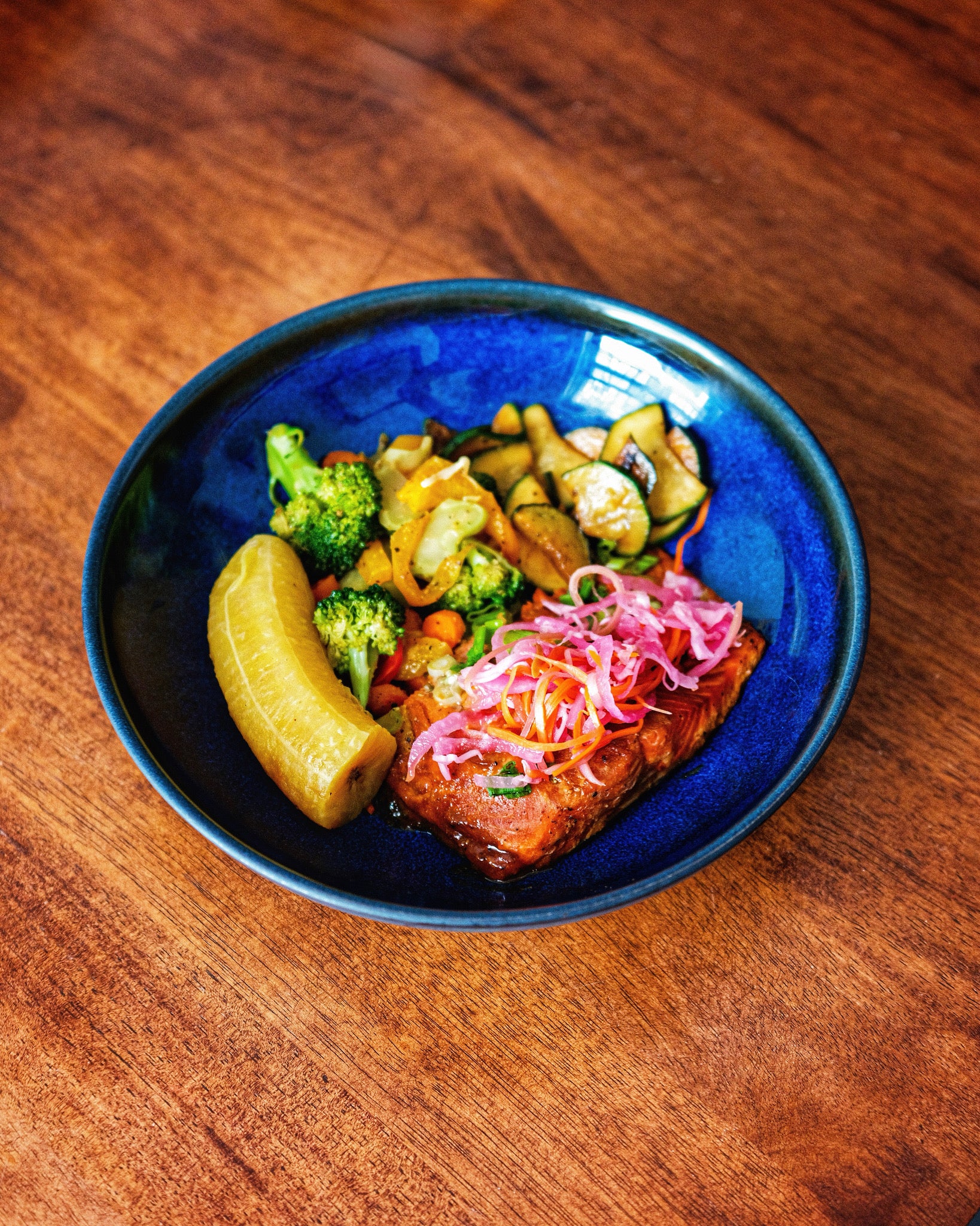 Blue bowl with grilled vegetables and salmon on a wooden table

