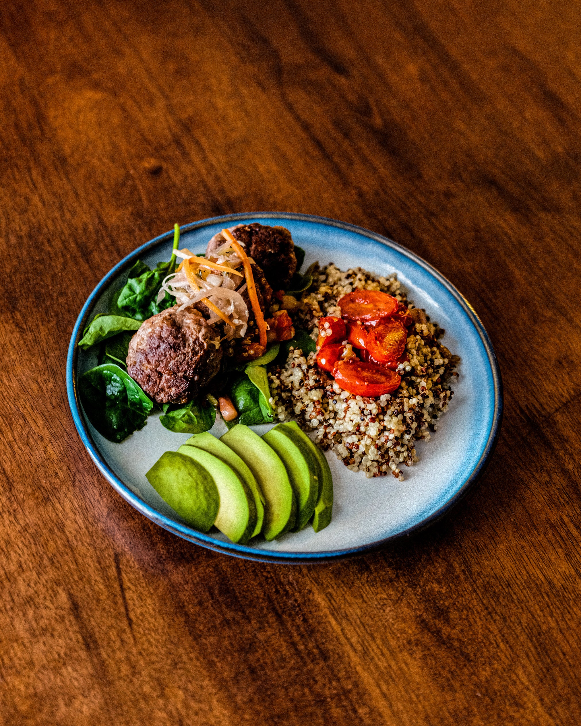 Plated meal with greens, quinoa, and sliced avocado on a wooden surface